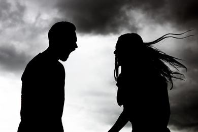 Image of Silhouettes of arguing couple against sky with heavy rainy clouds. Relationship problems