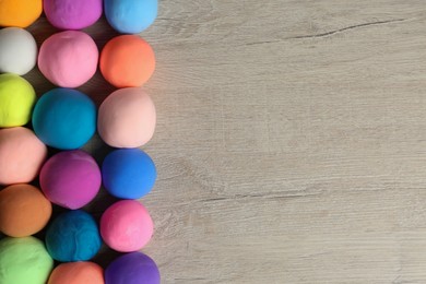Different color play dough balls on wooden table, flat lay. Space for text