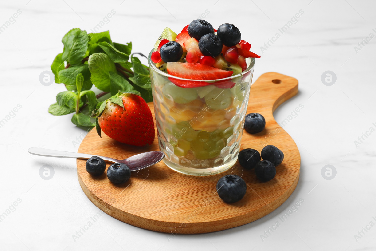 Photo of Healthy breakfast. Delicious fruit salad in glass and ingredients on white table
