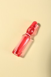 Photo of Glass ampoule with liquid on beige background, top view