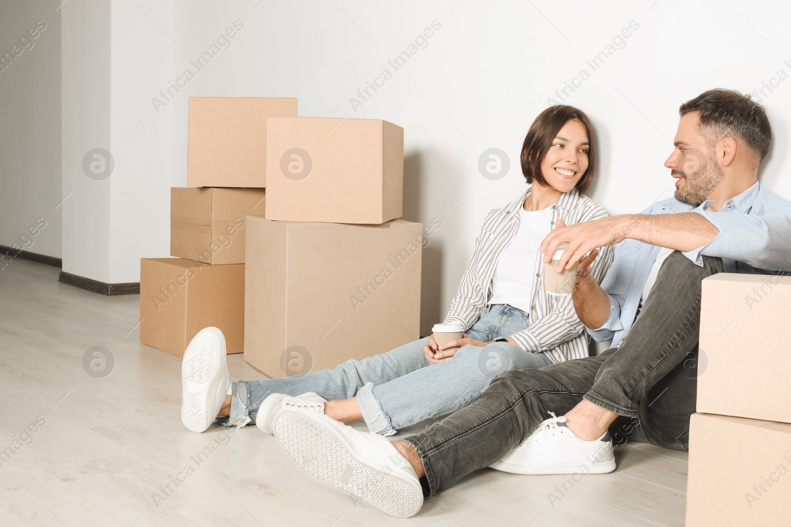 Photo of Happy couple with takeaway coffee resting on floor in new apartment. Moving day