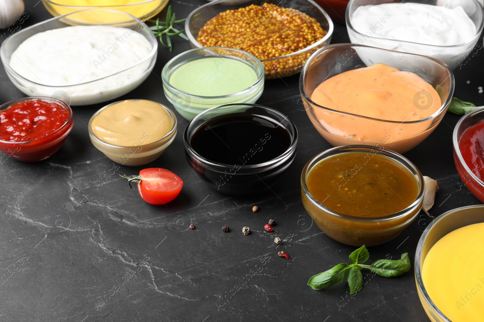 Photo of Many bowls with different sauces on black table