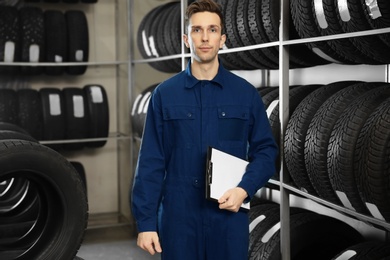 Photo of Young male mechanic with clipboard near tires in automobile service center