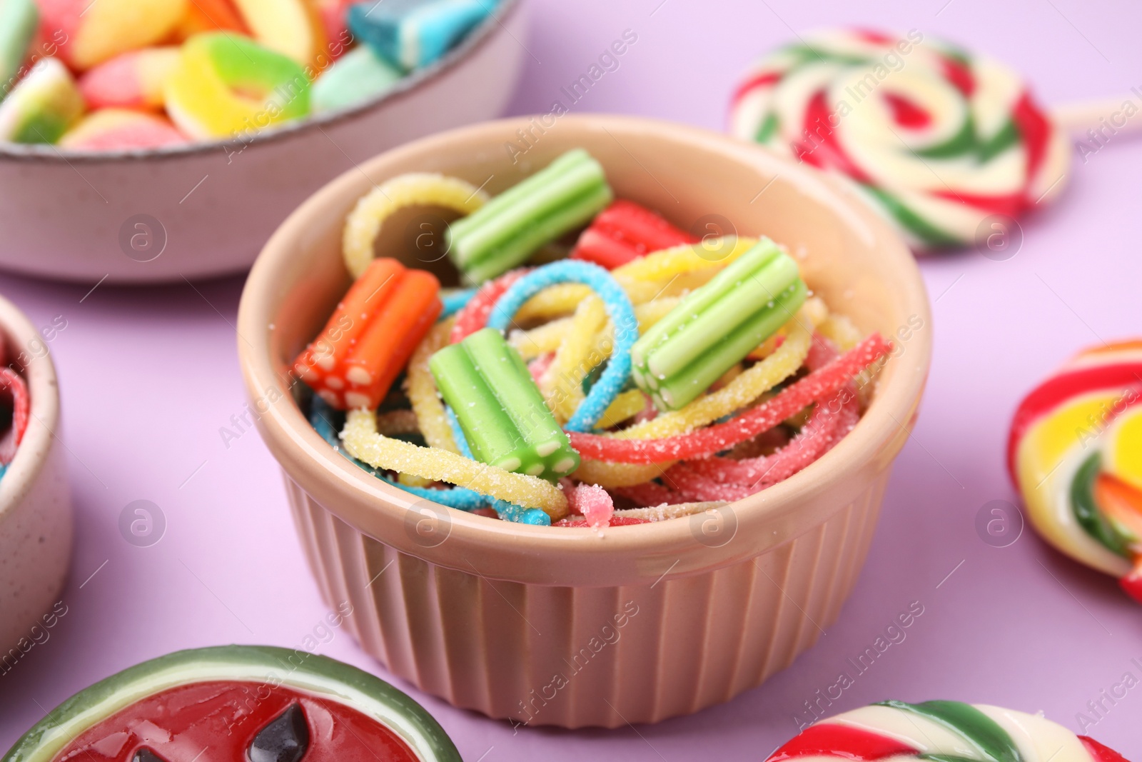 Photo of Bowl with different jelly candies on lilac background, closeup