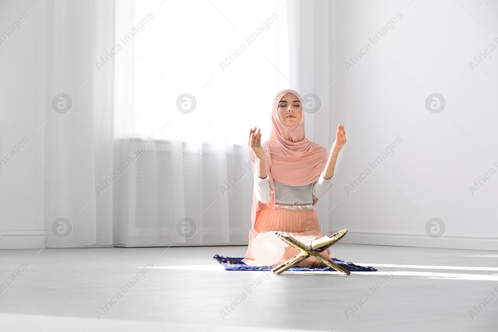 Photo of Muslim woman in hijab praying on mat indoors