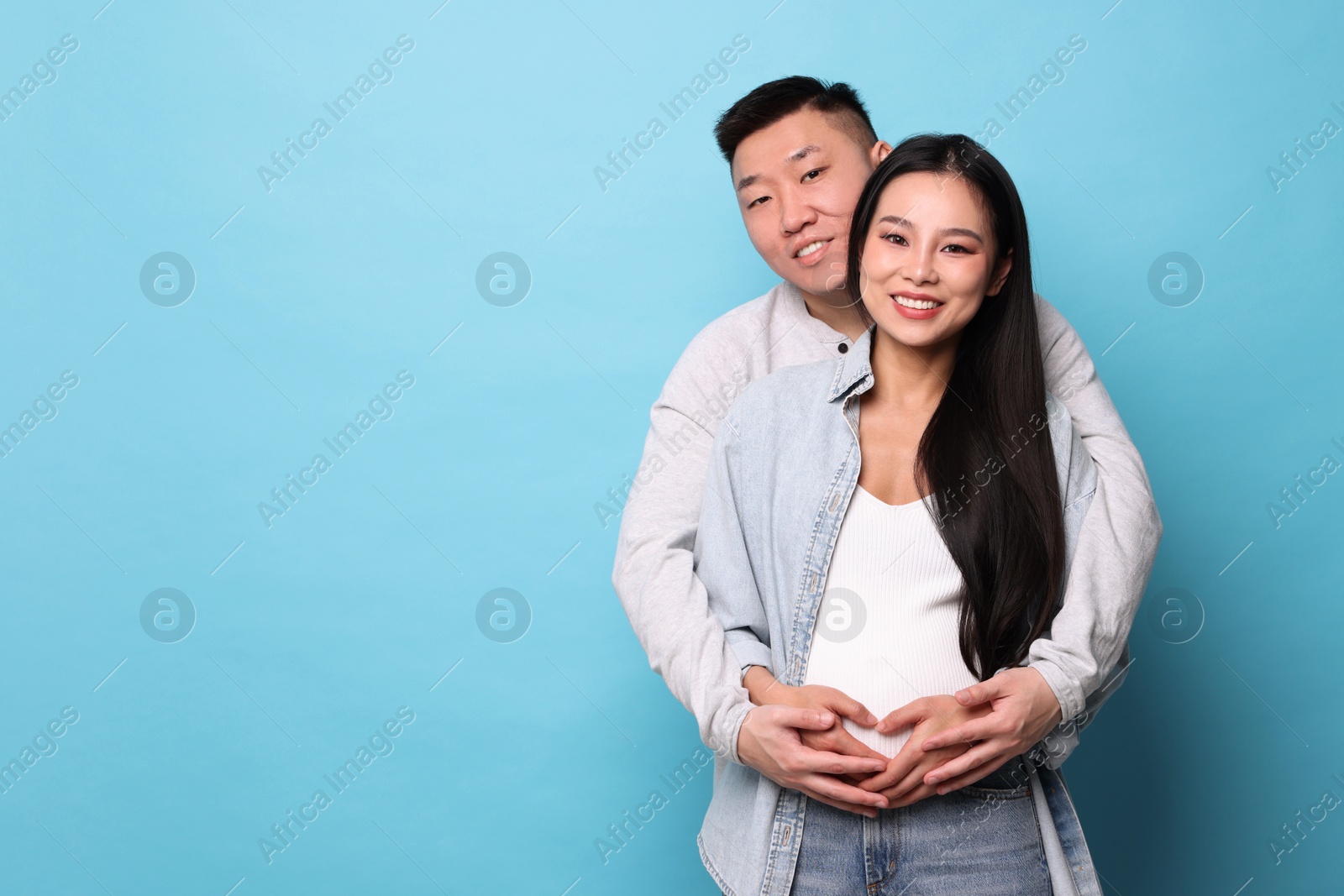 Photo of Man touching his pregnant wife's belly on light blue background, space for text