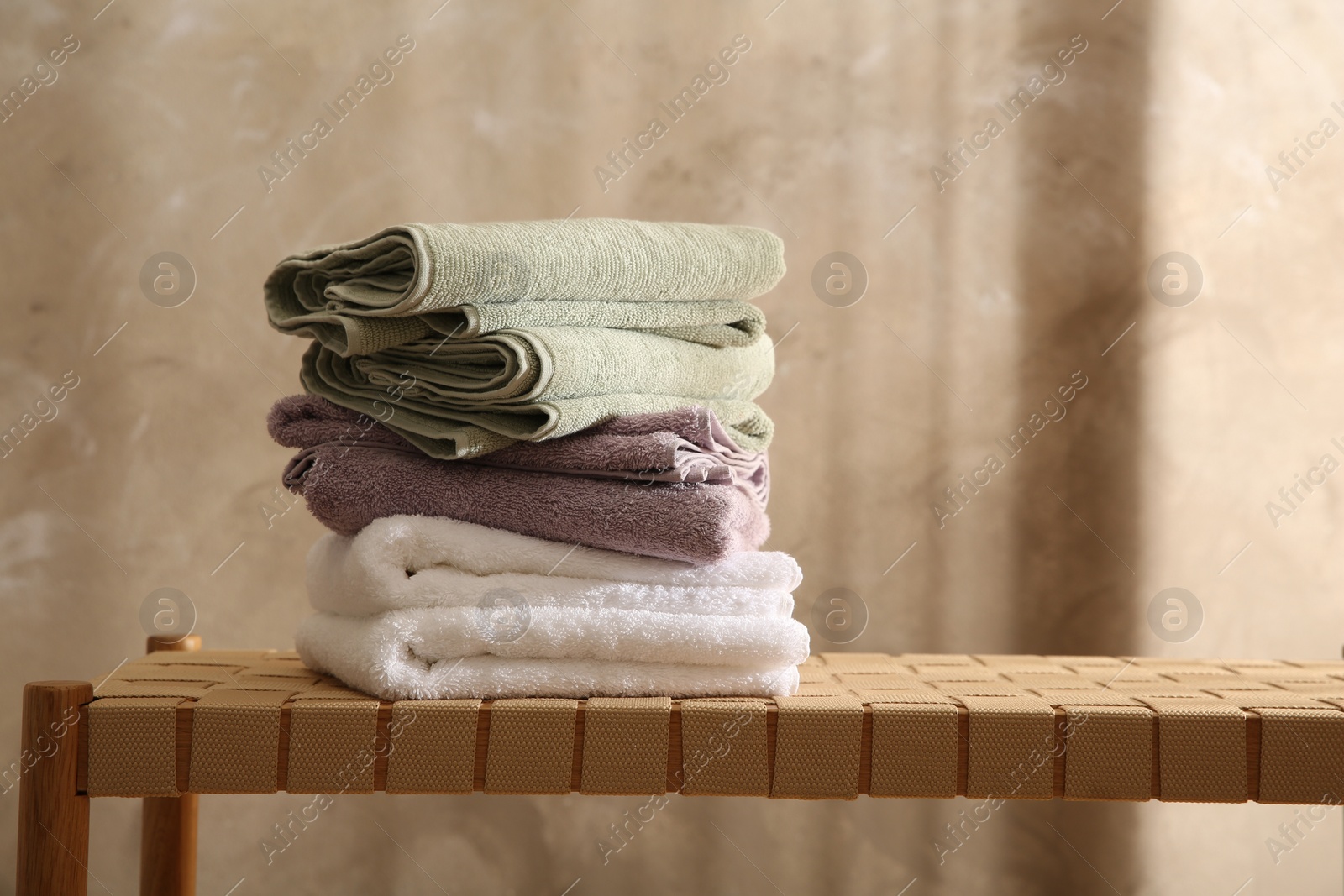 Photo of Stack of soft towels on wicker bench indoors