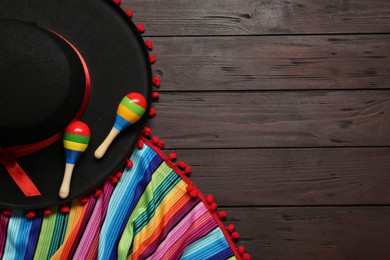 Photo of Mexican sombrero hat, maracas and colorful poncho on wooden background, flat lay. Space for text