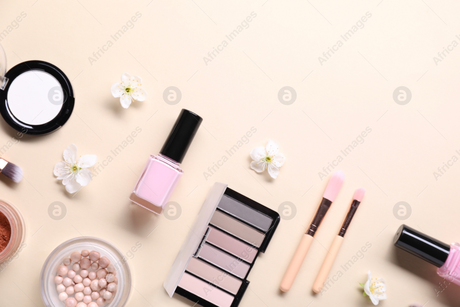 Photo of Flat lay composition with different makeup products and beautiful spring flowers on beige background, space for text