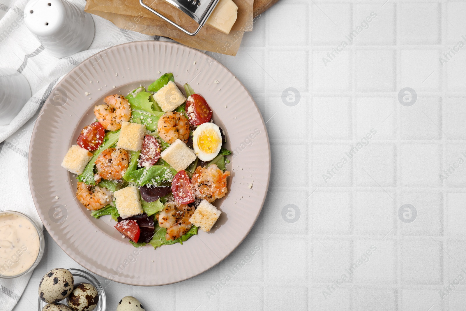 Photo of Delicious Caesar salad with shrimps and ingredients on white tiled table, flat lay. Space for text