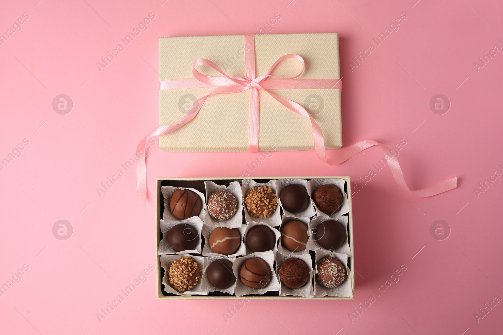 Photo of Box of delicious chocolate candies on pink background, flat lay