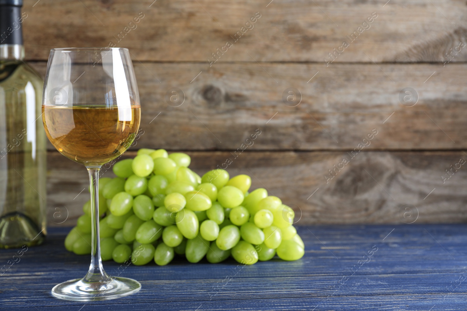 Photo of Fresh ripe juicy grapes and wine on blue table against wooden background. Space for text