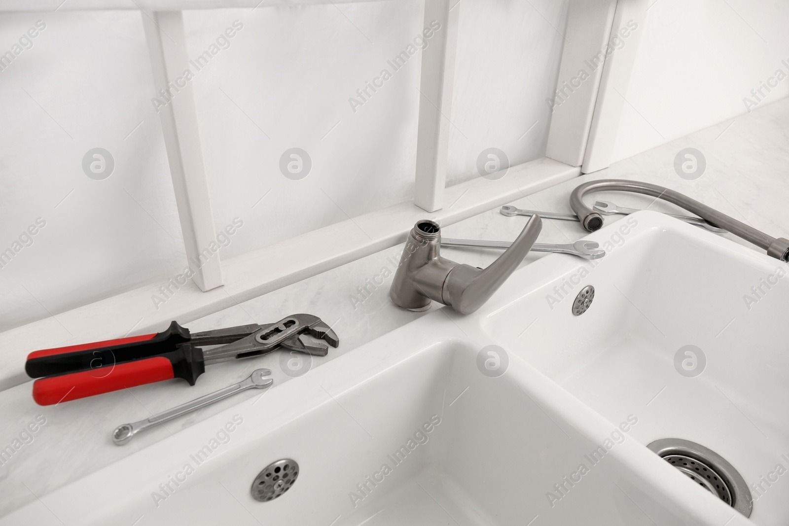 Photo of Plumber's tools and water tap ready for installation near sink on countertop in kitchen