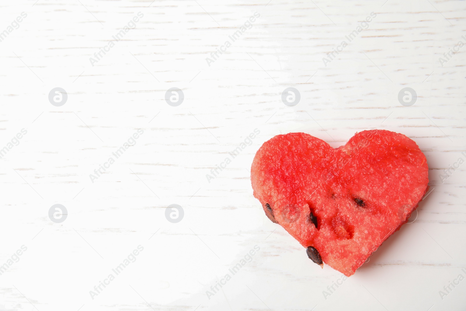 Photo of heart shaped watermelon slice on white wooden background, top view