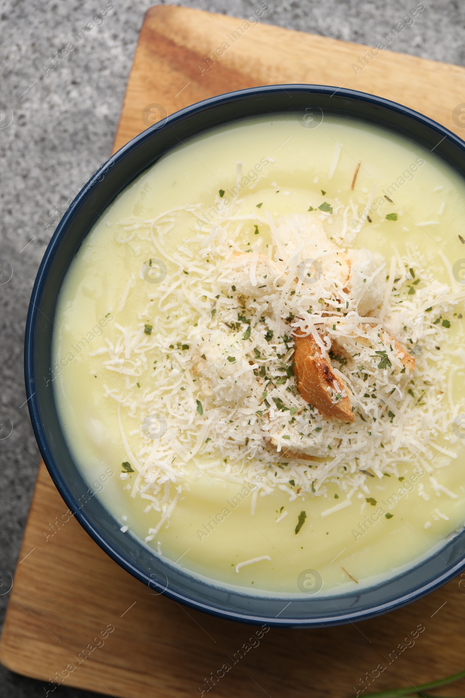 Photo of Delicious cream soup with parmesan cheese and croutons in bowl on grey table, top view