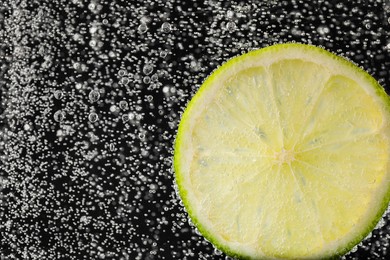 Juicy lime slice in soda water against black background, closeup