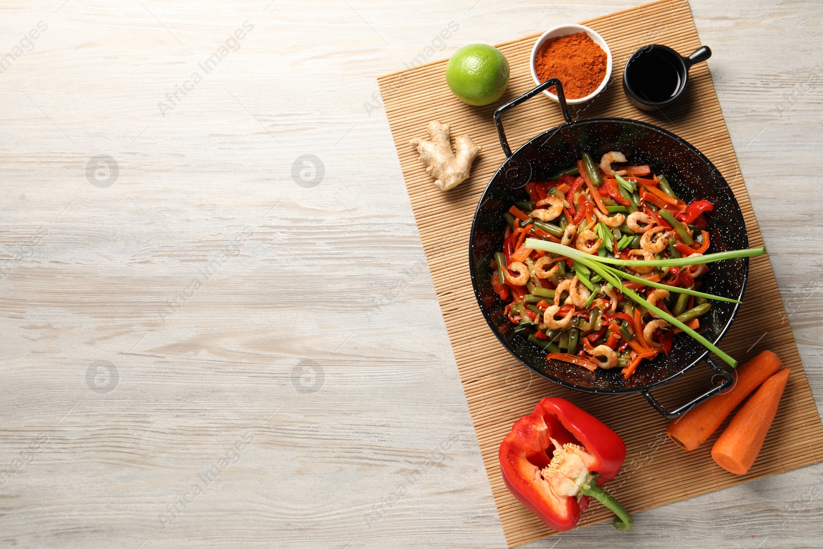 Photo of Shrimp stir fry with vegetables in wok and ingredients on wooden table, flat lay. Space for text