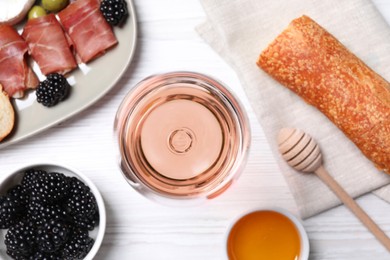 Glass of delicious rose wine and snacks on white wooden table, flat lay