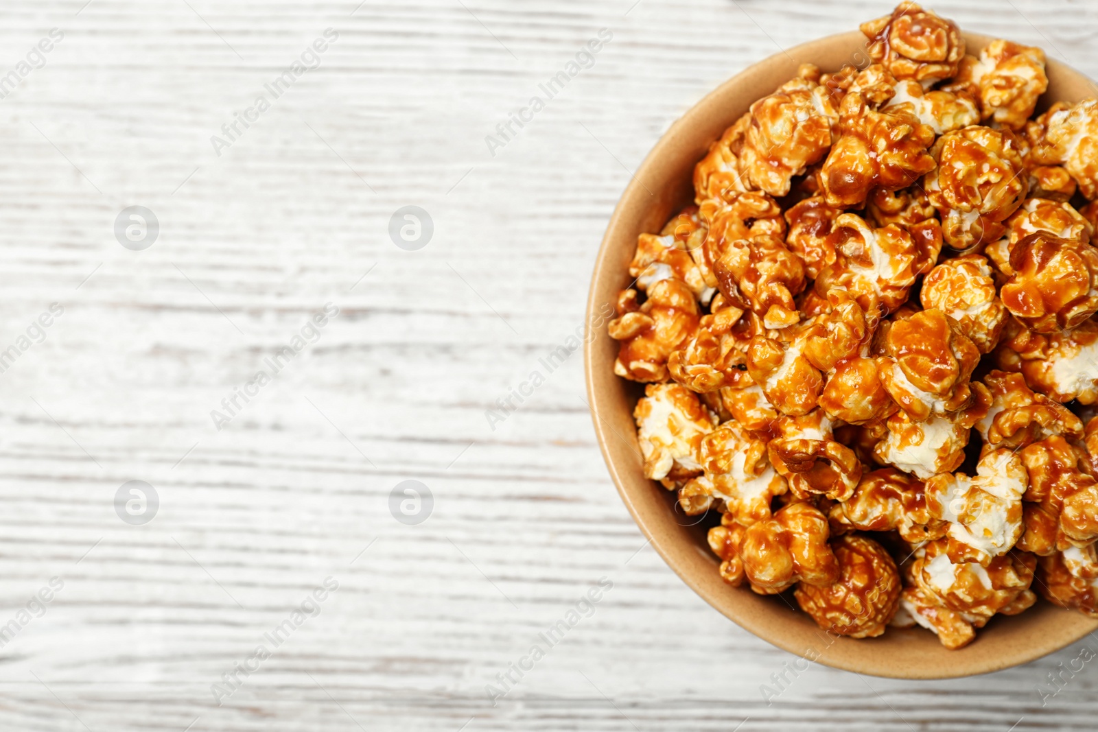 Photo of Bowl with caramel popcorn on white wooden background, top view. Space for text