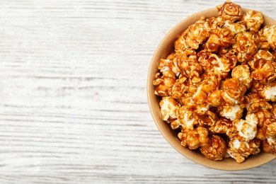 Photo of Bowl with caramel popcorn on white wooden background, top view. Space for text