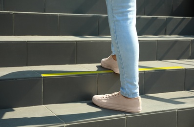 Photo of Woman standing on stairs with taped floor marking for social distance, closeup. Coronavirus pandemic