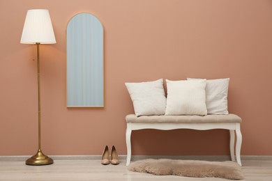 Room interior with white bench and mirror hanging on light pink wall. Stylish accessories