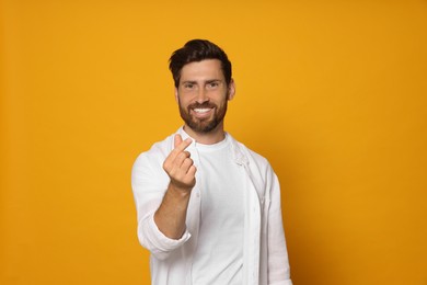 Photo of Handsome bearded man showing heart gesture on orange background