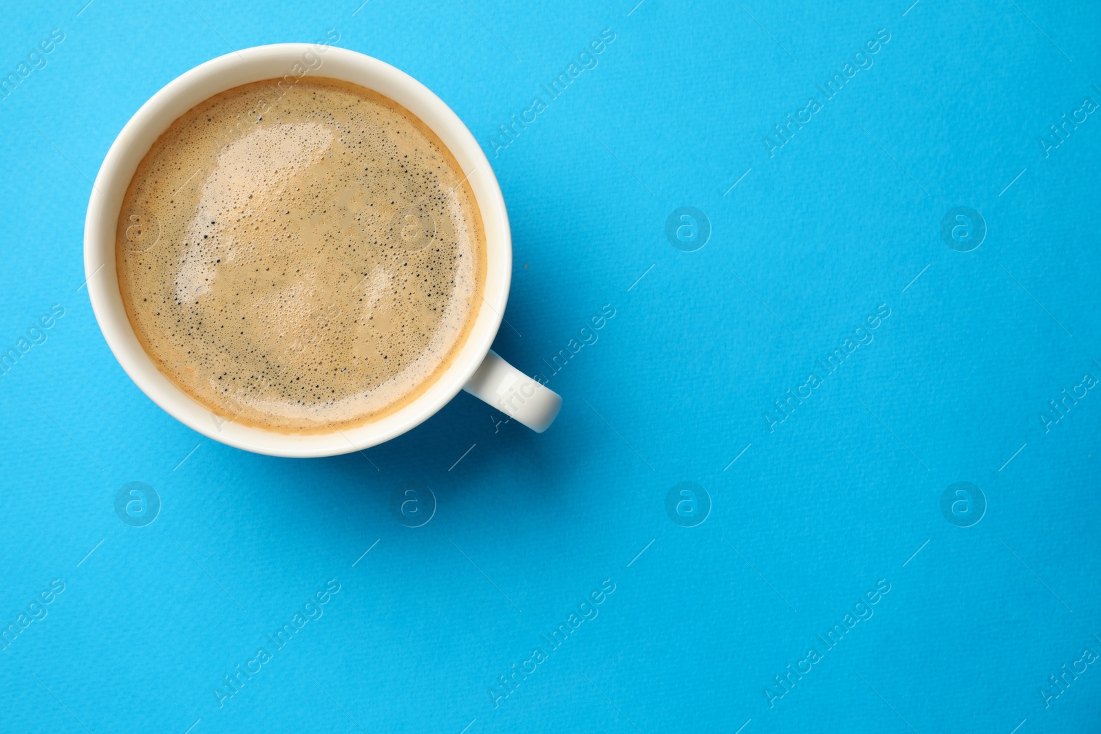 Photo of Aromatic coffee in cup on light blue background, top view. Space for text