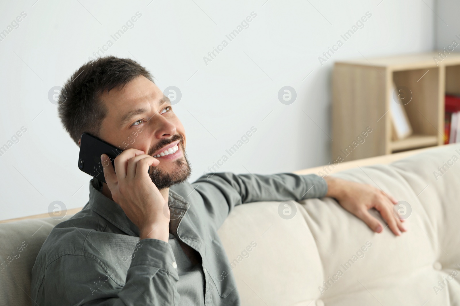 Photo of Happy man talking on smartphone at home