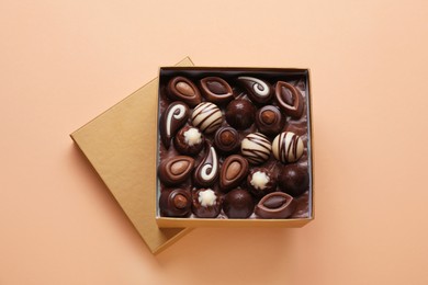 Photo of Open box of delicious chocolate candies on beige background, flat lay