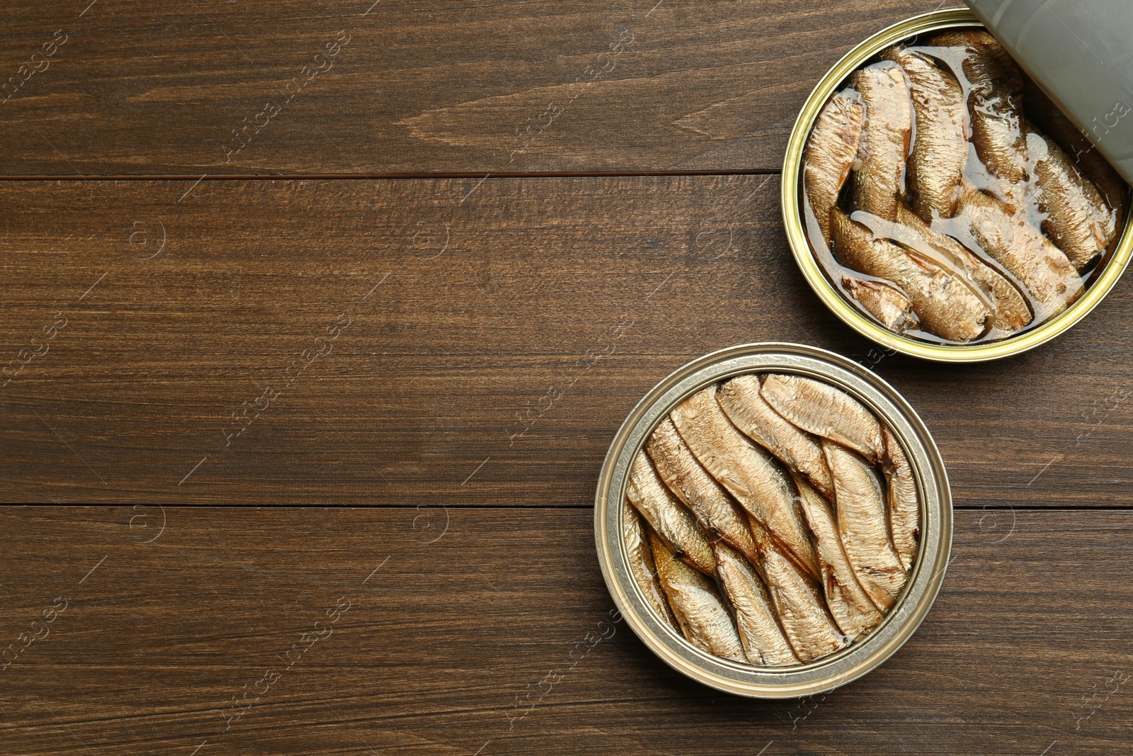 Photo of Open tin cans of sprats on wooden table, flat lay. Space for text