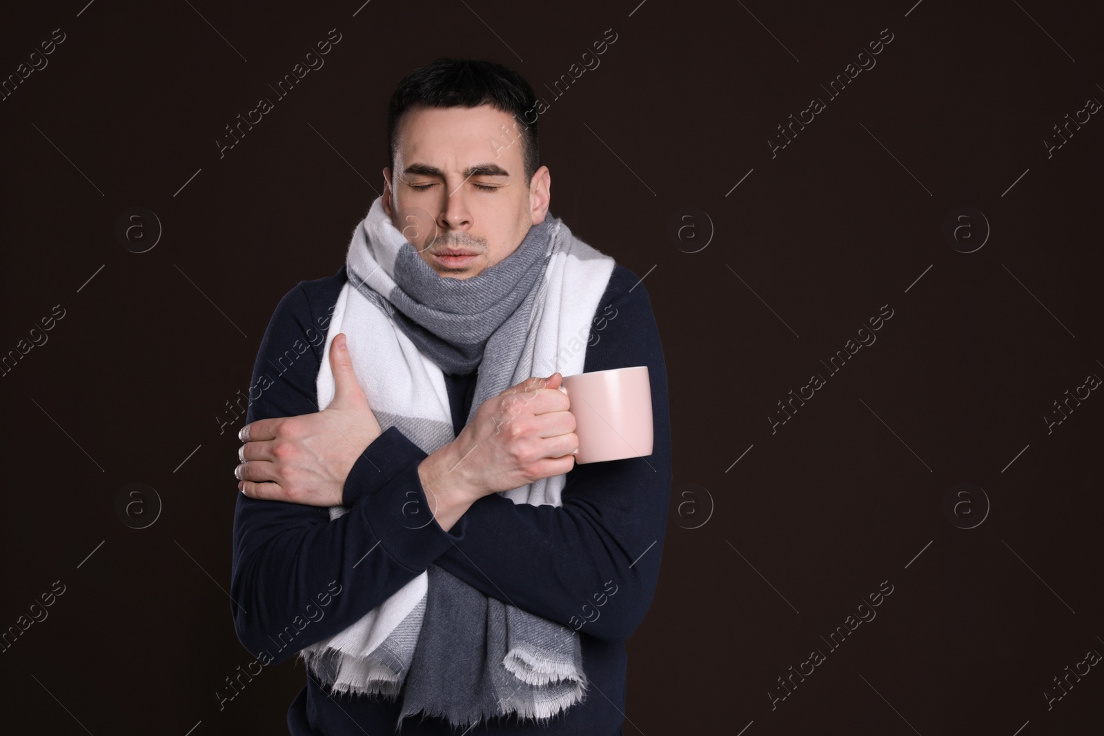 Photo of Young man with cup of hot drink suffering from fever on dark background, space for text. Cold symptoms