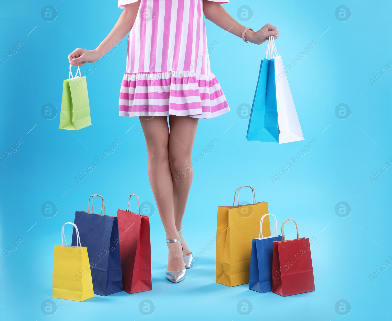 Photo of Young woman with shopping bags on color background, closeup of legs