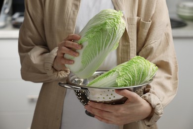 Woman holding fresh chinese cabbages in kitchen, closeup