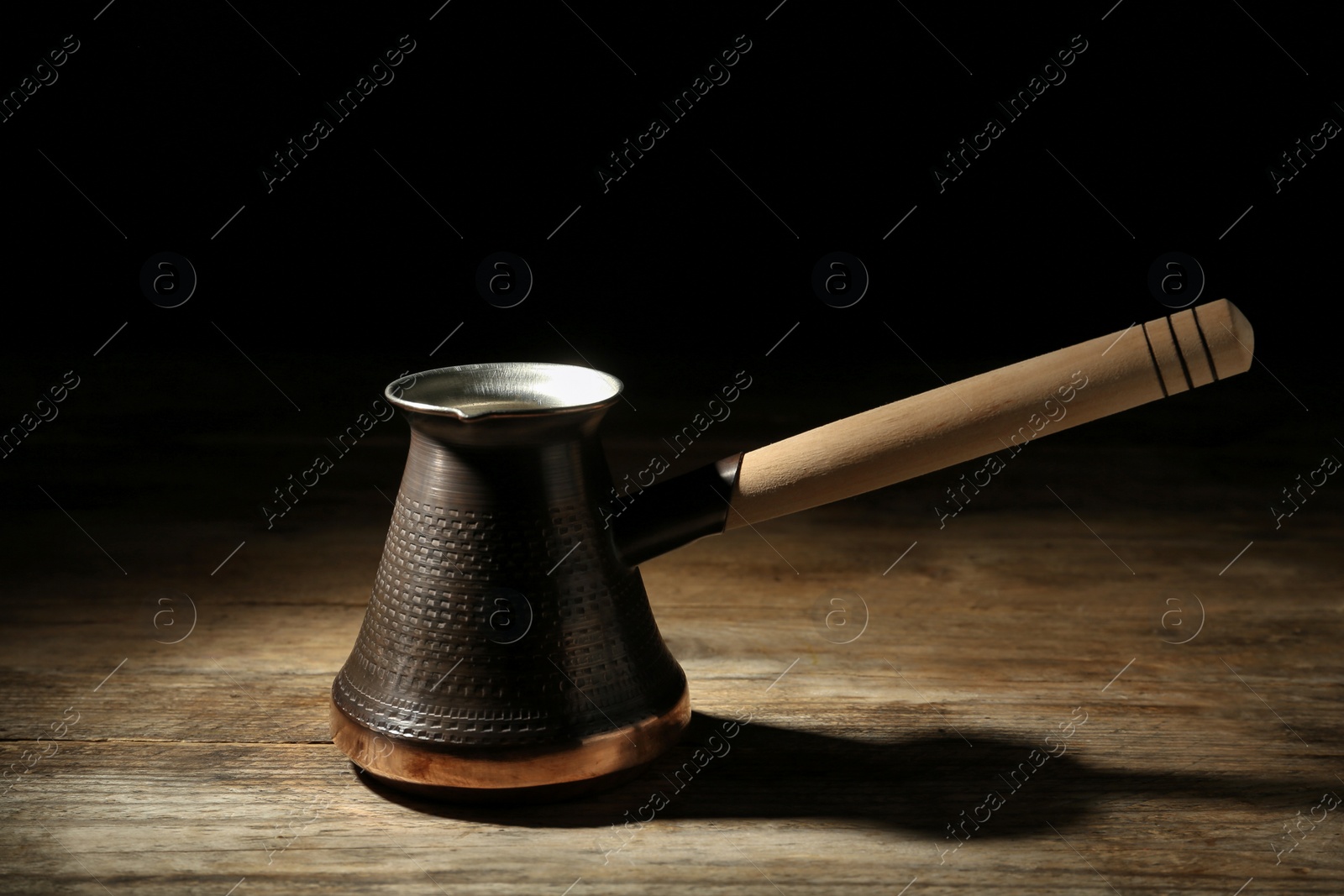 Photo of Beautiful copper turkish coffee pot on wooden table against dark background