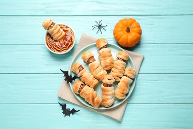 Photo of Spooky sausage mummies for Halloween party served on light blue wooden table, flat lay