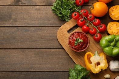 Delicious adjika sauce in bowl and ingredients on wooden table, flat lay. Space for text