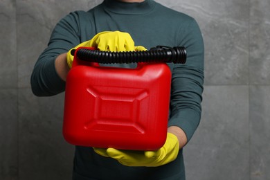Photo of Man in rubber gloves holding red canister near grey wall, closeup