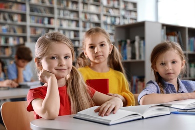 Happy little girls reading books at table in library