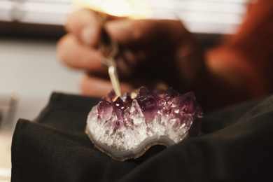Photo of Professional jeweler working with beautiful amethyst indoors, closeup