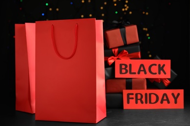 Photo of Paper shopping bags, gift boxes and phrase Black Friday against blurred lights