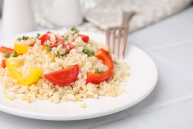 Photo of Plate of cooked bulgur with vegetables on white tiled table, closeup