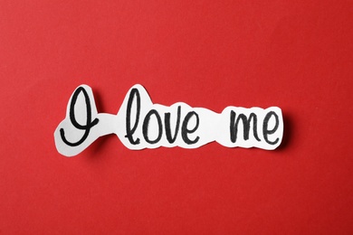 Piece of paper with handwritten phrase I Love Me on red background, top view