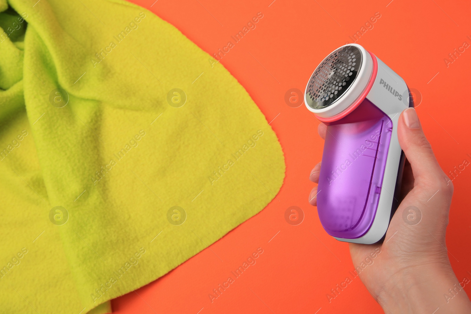 Photo of Woman with fabric shaver and light green cloth on orange background, closeup