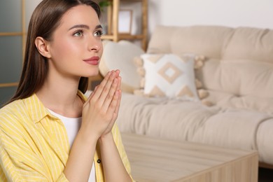 Woman with clasped hands praying at home, space for text