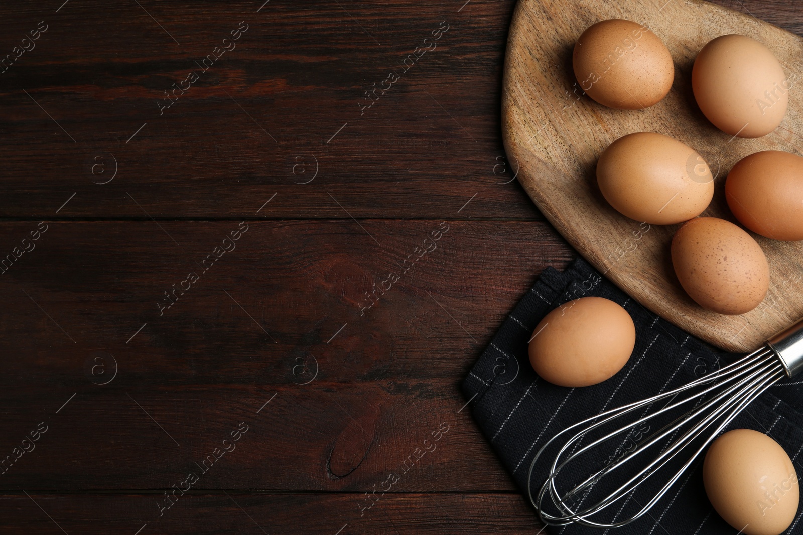 Photo of Chicken eggs and whisk on wooden table, flat lay. Space for text