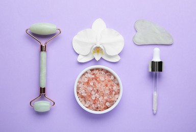 Flat lay composition with gua sha stone and face roller on violet background