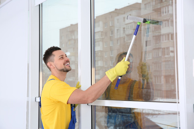 Professional janitor cleaning window with squeegee indoors