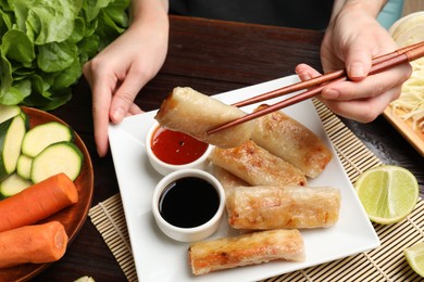 Woman eating tasty fried spring rolls at table, closeup