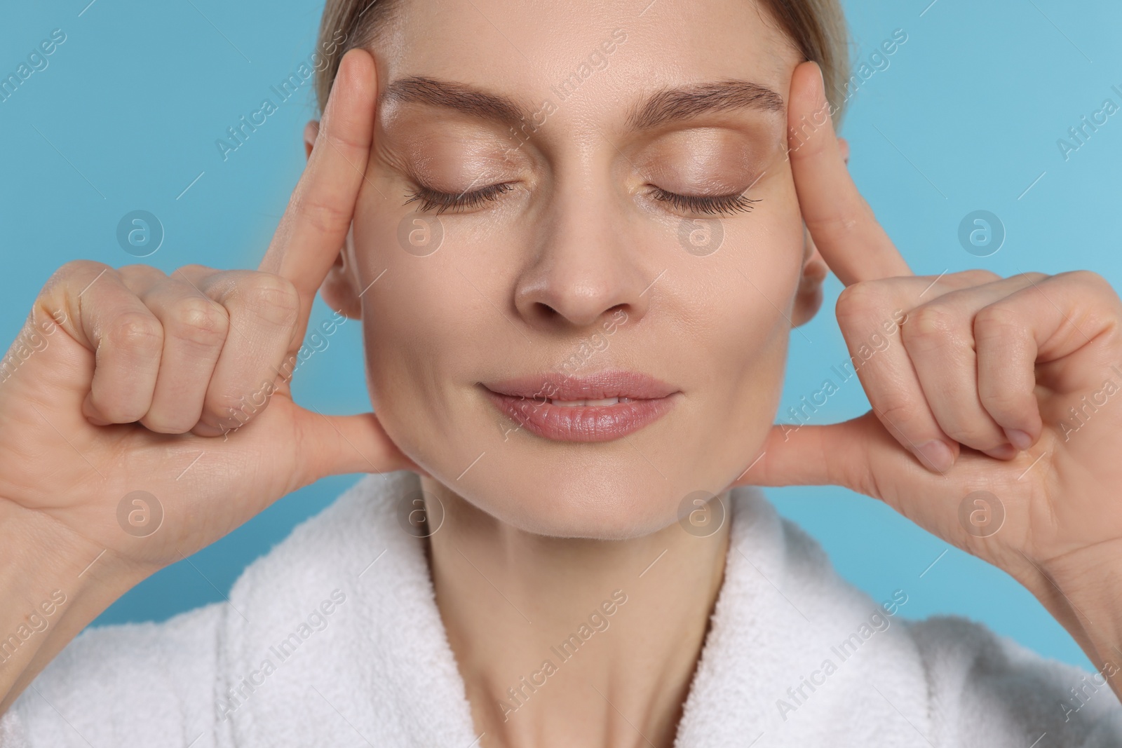 Photo of Woman massaging her face on turquoise background